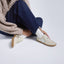 Person seating on the floor wearing the Balboa Sneaker in Ivory Nubuck, styled with dark blue jeans, beige sweater. and black and white polka dot socks