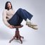 Woman siting on a stool with her legs in the air, wearing the Balboa Sneaker in Ivory Nubuck, styled with dark blue jeans, beige sweater. and black and white polka dot socks