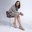 Woman sitting in a brown leather chair wearing a beige sweater dress and the Balboa Sneaker in metallic suede