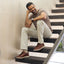 Man sitting on a staircase wearing Featherlight Fast Cognac leather shoes on a neutral background.