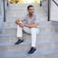 Man sitting on concrete steps wearing a light brown shirt, white pants, and featherlight fast navy shoes.