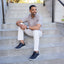 Man sitting on concrete steps wearing a light brown shirt, white pants, and featherlight fast navy shoes.