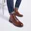 A person wearing featherlight lace-up ankle boots with dark soles and brass eyelets, paired with cuffed blue jeans, standing on a light gray studio floor.