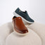 Featherlight Loafer in Cognac and Navy displayed on a round beige upholstered stool against a clean white background. 