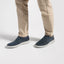 A person wearing beige trousers and dark navy Featherlight Loafers with light gray soles, shown from the knees down on a clean white studio background.