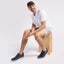 Man sitting on a wooden block wearing Featherlight Muir Navy Nubuck sneakers, white t-shirt, beige shorts, and black cap.