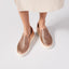 Rose gold slip-on sneakers with a white sole on a light gray background