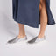 Silver slip-on shoes worn with a navy skirt on a plain background