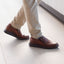 Rafael Slip-On cognac leather shoes worn with beige pants on a light wooden floor.