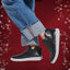 Black slip-on shoes worn with rolled-up jeans against a red background with bokeh lights
