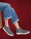 Person wearing gray slip-on shoes with rolled-up jeans on a red background